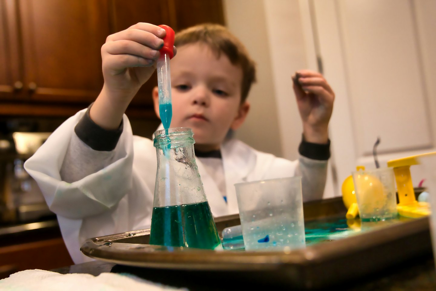 Niño con bata de laboratorio añade líquido azul a un matraz con cuentagotas.