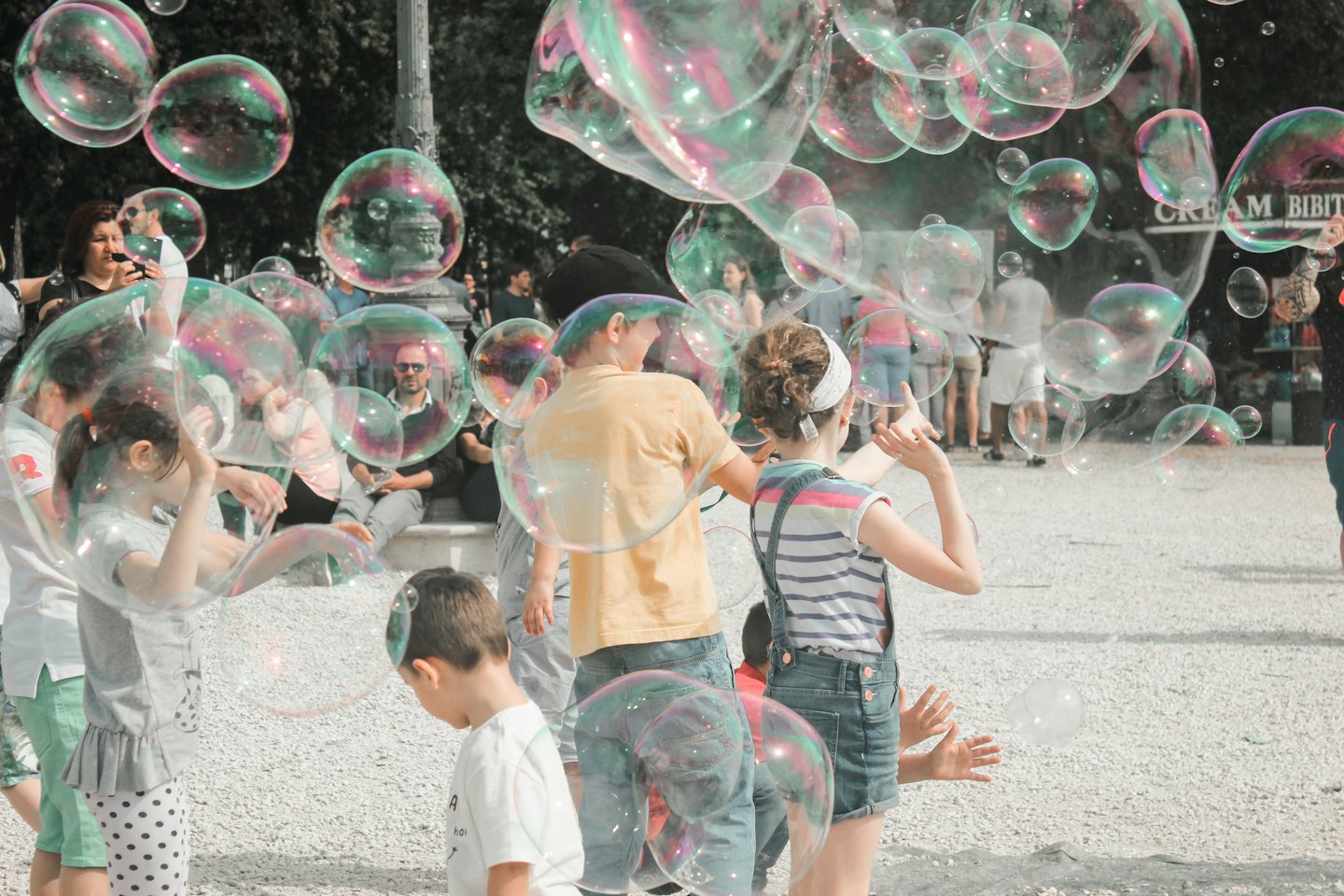Niños y adultos juegan con burbujas de jabón iridiscentes al aire libre.